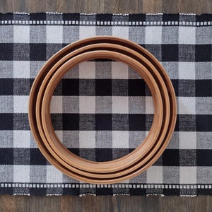 May include: Three nested circular wooden embroidery hoops with a smooth, light brown finish. The hoops are arranged concentrically, showing a consistent thickness and rounded edges, creating a simple, functional design for textile crafting projects.