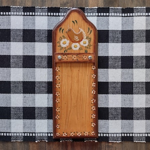 May include: Wooden wall-mounted organizer with a decorative painted design. The top features a brown bird and white daisies. The edges are adorned with small white flowers. A metal bar is secured with screws.