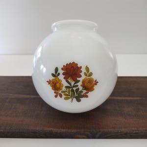 May include: A spherical white milk glass light fixture globe featuring a central floral decal. The design displays a cluster of stylized flowers in shades of orange, yellow, and brown with green leaves, centered on the smooth, opaque glass surface.