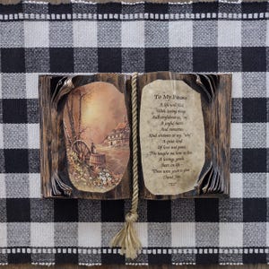 May include: A decorative open book sculpture with a dark brown wood-grain finish. The left page features a rustic landscape illustration with a house and wagon wheel. The right page displays the text To My Parents with a poem. A rope bookmark hangs down.