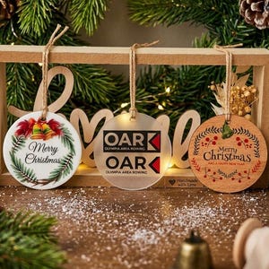 May include: Three circular hanging ornaments suspended from a wooden frame. The left is white with red bells and green holly. The center is frosted acrylic with black text reading OAR OLYMPIA AREA ROWING. The right is wood with red berries.