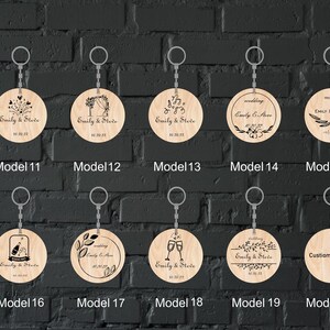 Op de afbeelding: Twintig verschillende ontwerpen voor ronde houten sleutelhangers. Elke sleutelhanger heeft een ander ontwerp met een huwelijksthema, waaronder bloemmotieven, muzieknoten en een champagnetoast. De sleutelhangers zijn gepersonaliseerd met de namen "Emily & Steve" en een huwelijksdatum.