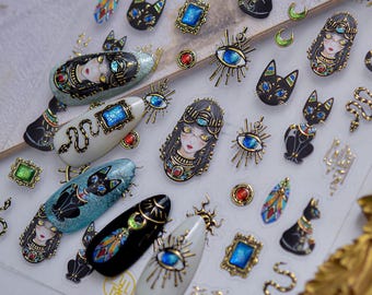 May include: A sheet of adhesive nail art stickers featuring Egyptian-inspired motifs including stylized cats, pharaoh portraits, blue gemstone frames, golden snakes, crescent moons, and sunburst eye symbols in vibrant colors and metallic gold accents.