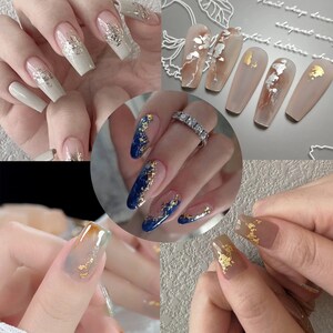 May include: Close-up of several manicured hands with different nail art designs. Some nails are painted with a dark blue base and gold glitter, while others have a clear base with gold leaf accents.