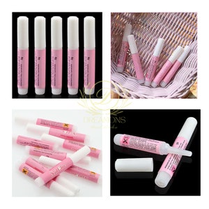 May include: Multiple tubes of nail glue with white caps and pink labels. The labels include the text "Nail Glue" and ingredient information. The glue tubes are displayed in various arrangements, including a close-up of a single tube with its cap off.