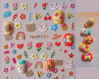 May include: A sheet of colourful nail stickers with a variety of designs, including hearts, flowers, rainbows, bears, bunnies, and the word "Happy".