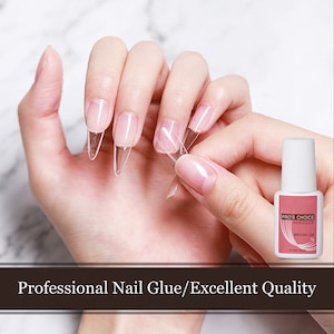 Op de afbeelding: Een doorzichtige fles nagellijm met een roze etiket waarop "Pro's Choice Nail Glue" en "Brush-On 7g" staat. De fles wordt vastgehouden door een hand met doorzichtige nageltips op de vingers.