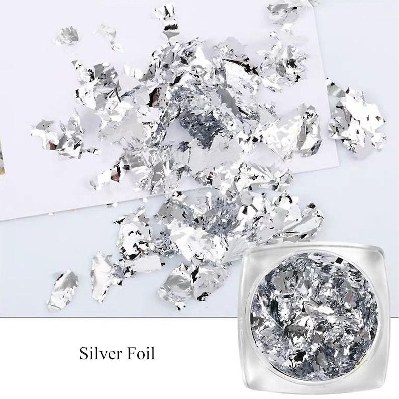 May include: A clear jar filled with silver foil flakes. The foil is scattered around the jar on a white surface. The text "Silver Foil" is printed below the jar.