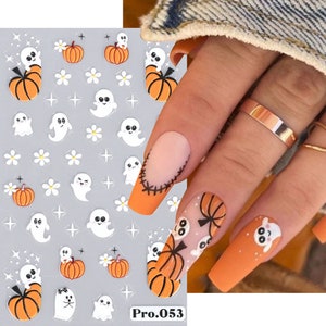 May include: Halloween-themed nail art stickers featuring orange pumpkins, white ghosts, and small white flowers on a gray background. The stickers are shown on a nail with an orange base and a ghost design. The text "Pro.053" is visible.