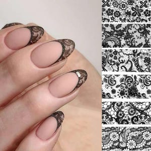 Op de afbeelding: Zwarte kant nagel stickers voor nail art. De stickers hebben verschillende kant patronen, waaronder bloemen en geometrische ontwerpen. De stickers worden getoond op een set naakte nagels.