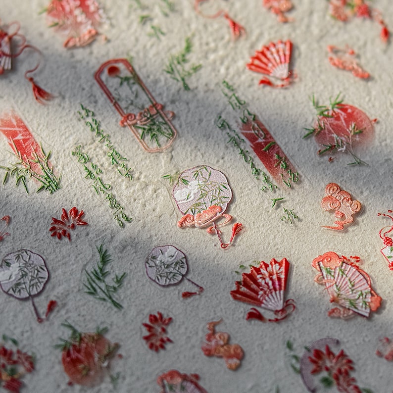 K&ouml;nnte beinhalten: Eine Blatt mit transparenten Aufklebern mit verschiedenen Designs, darunter F&auml;cher, Bambus und Blumen. Die Aufkleber sind in Rot-, Wei&szlig;- und Gr&uuml;nt&ouml;nen gehalten.