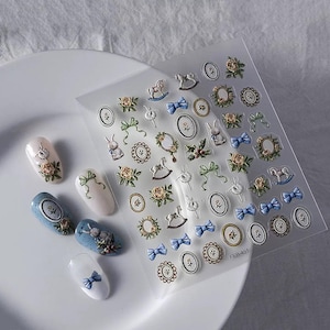 Puede incluir: Una lámina de pegatinas para uñas con diseños de estilo vintage, que incluyen caballos balancín, lazos, coronas florales y conejos. Se muestran varias uñas decoradas, mostrando los diseños de las pegatinas. Las pegatinas están sobre un fondo transparente.