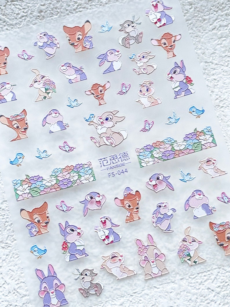Peut inclure: Une feuille de papier autocollant transparent avec une vari&eacute;t&eacute; d'autocollants de dessins anim&eacute;s color&eacute;s repr&eacute;sentant Bambi et Panpan. Les autocollants sont dispos&eacute;s en rang&eacute;es et comprennent des images des personnages avec des fleurs, des oiseaux et des papillons. Le texte "花边贴 - FANSIDE - FS-044" est imprim&eacute; sur la feuille.