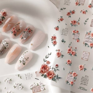 Puede incluir: Pegatinas de arte de u&ntilde;as con rosas rojas y blancas, hojas y escritura sobre un fondo transparente. Varias u&ntilde;as manicuradas est&aacute;n decoradas con el mismo dise&ntilde;o floral. Las pegatinas incluyen el texto "LOVE & ROSES" y "KX300".