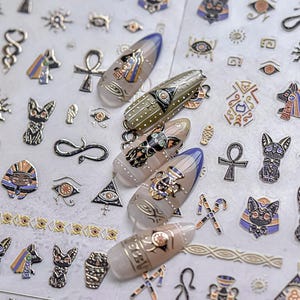 Peut inclure: Une feuille d'autocollants pour ongles de couleur or et noir avec des motifs sur le thème égyptien. Les motifs comprennent un œil d'Horus, un ankh, un scarabée et un chat.