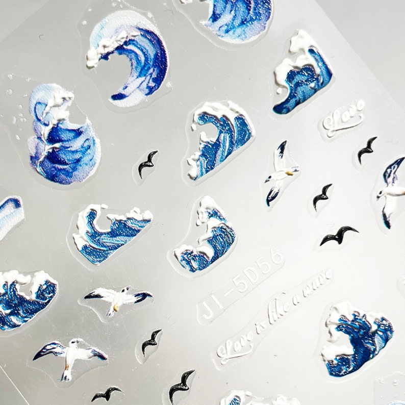 May include: A sheet of clear nail stickers with blue and white wave designs and black seagull and bird silhouettes. The sheet also includes the text "Love is like a wave" and "JJ-5D56".