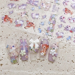 Peut inclure: Six pointes d'ongles transparentes avec diff&eacute;rents motifs d'art d'ongles de personnages Disney. Les motifs comprennent un n&oelig;ud blanc, un cerf brun, un lapin violet, un lapin blanc et deux motifs floraux.
