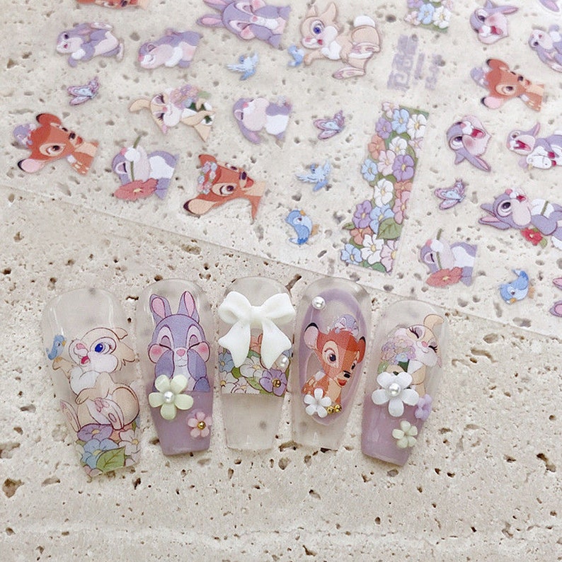 Peut inclure: Six pointes d'ongles transparentes avec diff&eacute;rents motifs d'art d'ongles de personnages Disney. Les motifs comprennent un n&oelig;ud blanc, un cerf brun, un lapin violet, un lapin blanc et deux motifs floraux.