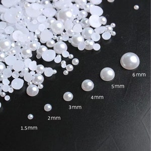 May include: Assortment of white pearl beads in various sizes, ranging from 1.5 mm to 6 mm. The beads are displayed on a black surface with size labels in millimetres.