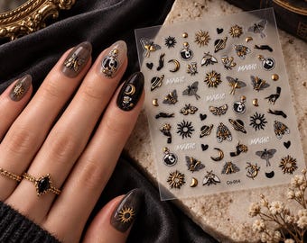 May include: A sheet of adhesive nail decals featuring gold and black designs of moths, suns, moons, planets, potion bottles, and hands. The word MAGIC is printed in white script throughout the sheet, which also includes the text Co-054 at the bottom.