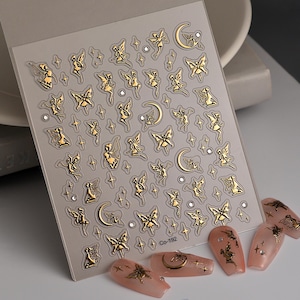 May include: Gold nail art stickers featuring fairies, butterflies, moons, and stars. The stickers are on a clear sheet with a white background. The sheet has the text "Co-192" printed on it.