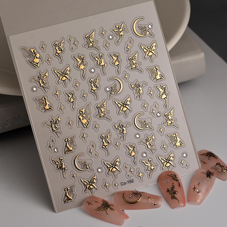May include: Gold nail art stickers featuring fairies, butterflies, moons, and stars. The stickers are on a clear sheet with a white background. The sheet has the text "Co-192" printed on it.
