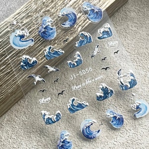 May include: A sheet of clear nail stickers with blue and silver waves and seagulls. The sheet has the text "Love is like a wave" and "JI-5D56" printed on it.