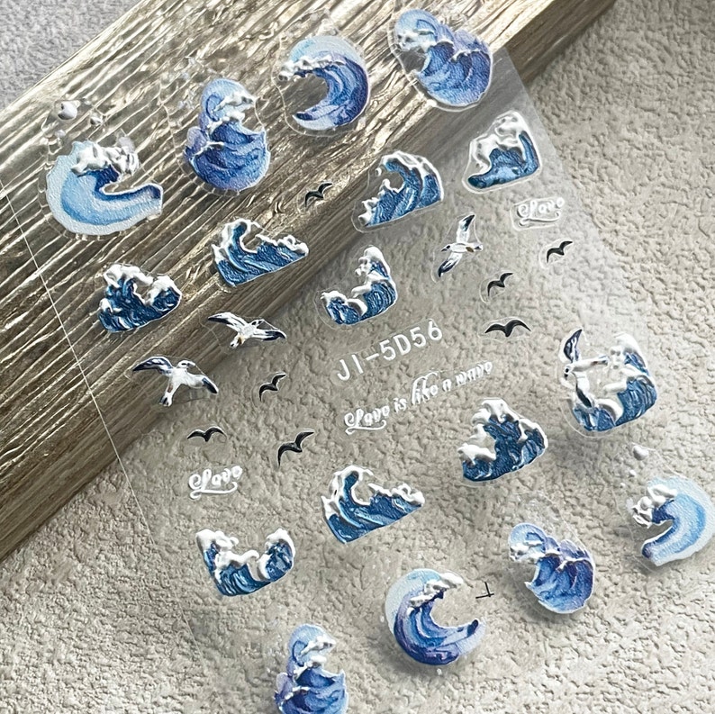 May include: A sheet of clear nail stickers with blue and silver waves and seagulls. The sheet has the text "Love is like a wave" and "JI-5D56" printed on it.