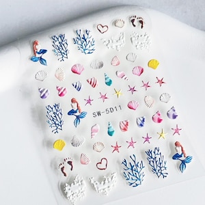 Könnte beinhalten: Transparente Folie mit Nagelkunst-Aufklebern mit Meerjungfrauen, Muscheln, Seesternen, Korallen und Fußabdrücken. Die Aufkleber sind in verschiedenen Farben, darunter Rosa, Blau, Gelb und Weiß. Der Text "SW-5D11" ist aufgedruckt.