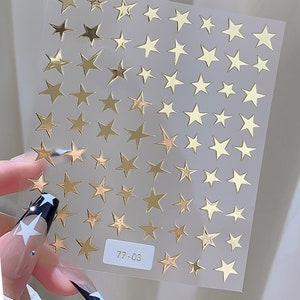 May include: A sheet of gold star stickers on a clear background. The sheet has 77-03 printed on it.