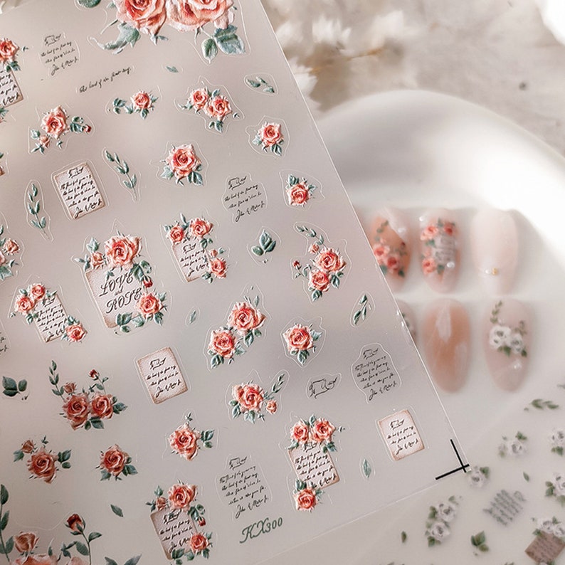 Puede incluir: Pegatinas transparentes para decoraci&oacute;n de u&ntilde;as con un dise&ntilde;o floral de rosas, las palabras "Love Rose" y texto escrito. Las pegatinas tienen un efecto 3D y son en tonos rojos, rosas y verdes. La imagen tambi&eacute;n muestra u&ntilde;as manicuradas con dise&ntilde;os florales similares.