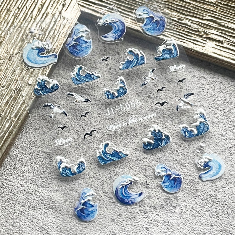 May include: A sheet of clear nail stickers with blue and white wave designs and small black and white seagull designs. The sheet has the text "JI-5D56" and "Love is the answer" printed on it.