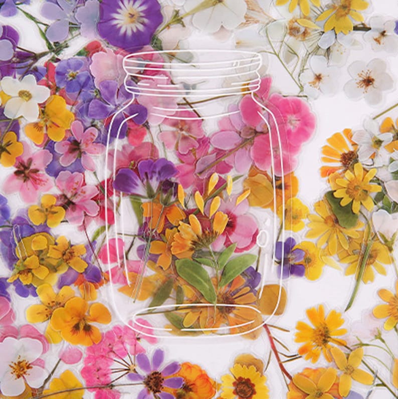 May include: A clear glass jar filled with pressed flowers in various colors, including yellow, pink, purple, and white. The jar is outlined in white and has a lid.