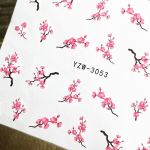 May include: A sheet of nail art stickers with a white background and pink cherry blossom designs. The text "YZW-3053" is printed on the sheet.