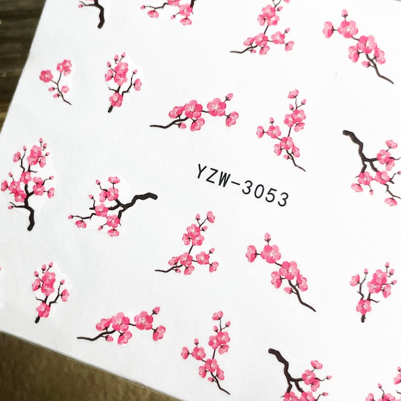 May include: A sheet of nail art stickers with a white background and pink cherry blossom designs. The text "YZW-3053" is printed on the sheet.