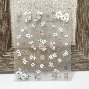 Puede incluir: Hoja de pegatinas transparente con ilustraciones de rosas blancas y texto. La hoja incluye rosas de varios tama&ntilde;os, ramitas y dise&ntilde;os rectangulares con escritura y las palabras "LOVE and ROSE".