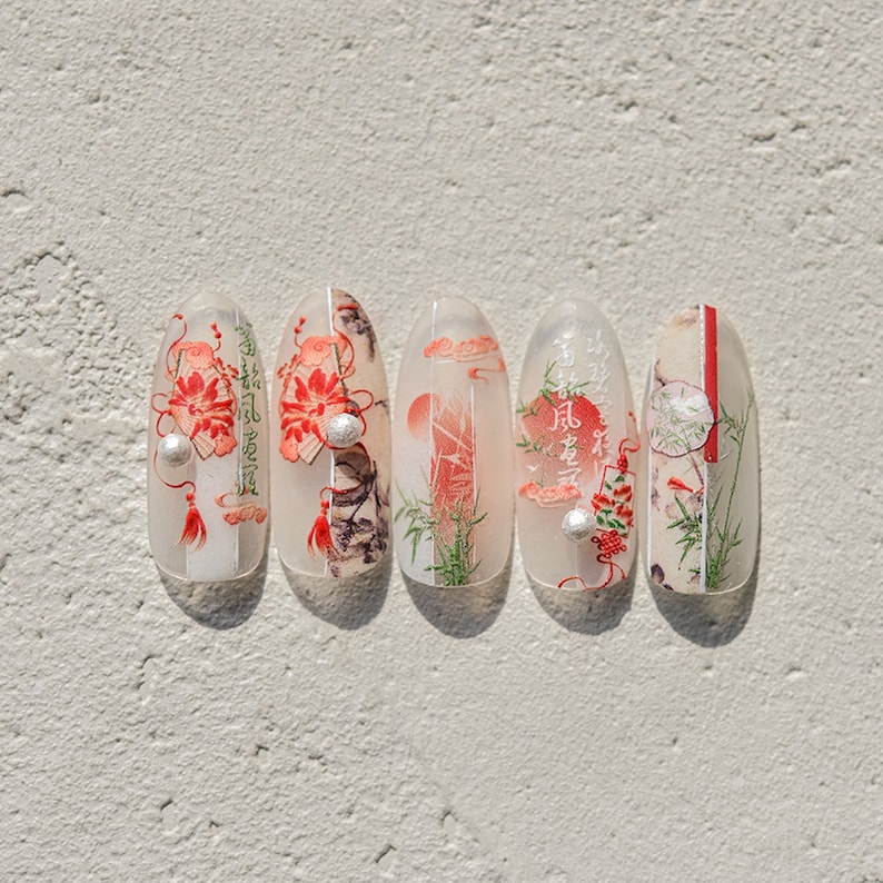 K&ouml;nnte beinhalten: F&uuml;nf ovale Nageldesigns mit wei&szlig;em Hintergrund und roten, schwarzen und gr&uuml;nen Akzenten. Die Designs zeigen japanische Schriftzeichen, Blumen und Bambus.