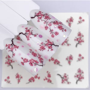 May include: Nail art stickers with a white background and pink cherry blossom designs. The stickers are arranged in a pattern of three rows, with each row containing three stickers.