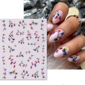 May include: A sheet of nail art stickers with a design of colorful Christmas lights. The sheet is white with a black border and the text "SW-5D113" printed on it.