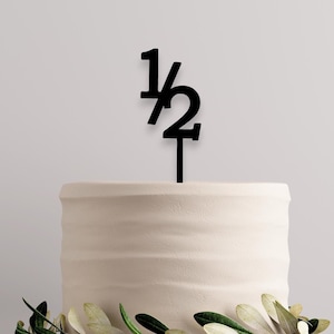 May include: A white cake with a black acrylic cake topper that says "1/2"