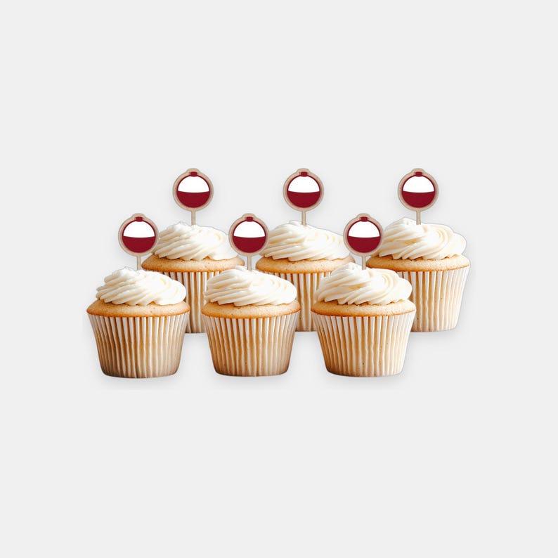 May include: Six vanilla cupcakes with white swirled frosting, each topped with a circular paper topper featuring a red and white fishing bobber graphic on a thin wooden pick. The cupcakes are arranged in two rows, with three in the front and three in the back.