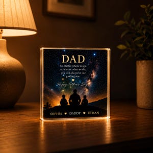 以下が含まれることがあります： 上部に「DAD」の文字が入った、星空のデザインと父と2人の子供のシルエットが特徴の、光るアクリルブロック。「Happy Father's Day」の文字と、下に名前が書かれています。
