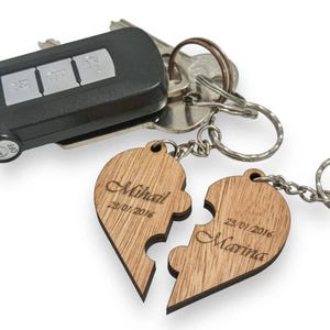 Puede incluir: Dos piezas de rompecabezas de madera en forma de corazón con los nombres Mikhail y Marina grabados en ellas, junto con las fechas 23/01/2016 y 23/01/2016. Las piezas están unidas a un llavero plateado.