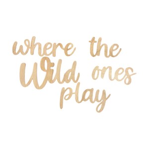 May include: Wooden wall art with the phrase "where the wild ones play" in a cursive font. The letters are cut from light-colored wood and arranged on a white background. Ideal for a nursery or children's room.