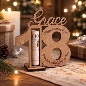 May include: A wooden birthday gift with the name "Grace" and the number "18" cut out. A rolled-up £10 note is visible. The text "Happy Birthday to you!" and "Love from, Avril, Gary & Rory" are engraved on the wooden frame.