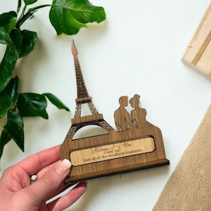 Könnte beinhalten: Holzskulptur des Eiffelturms mit einem Paar, das davor steht. Die Skulptur trägt eine personalisierte Inschrift mit dem Text "Helena & Alex Ich liebe dich mehr als alle Waldwesen."