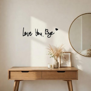 Puede incluir: Arte mural negro en cursiva que dice "Love You, Bye" con un símbolo de corazón. El arte está montado en una pared blanca sobre una consola de madera.