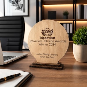 May include: A wooden TripAdvisor Travellers' Choice Awards Winner 2024 plaque. The plaque is light brown with dark brown text and a logo. The base is a darker brown. The text reads "Autism Friendly Caravans Haven Cala Gran".