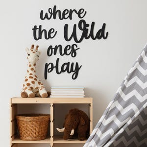 May include: A wooden shelf holds a stuffed giraffe, a woven basket, a stuffed mammoth, and a stack of books. The wall above features black cursive text that reads "where the Wild ones play". A gray and white chevron patterned tent is in the background.