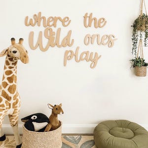 May include: A nursery scene with a giraffe plush toy, a woven basket with stuffed animals, and wooden wall art that reads "where the wild ones play." Hanging plants and a green beanbag chair complete the room's decor.